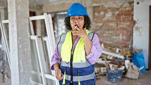 Young beautiful latin woman builder smoking cigarette with serious face at construction site © Krakenimages.com