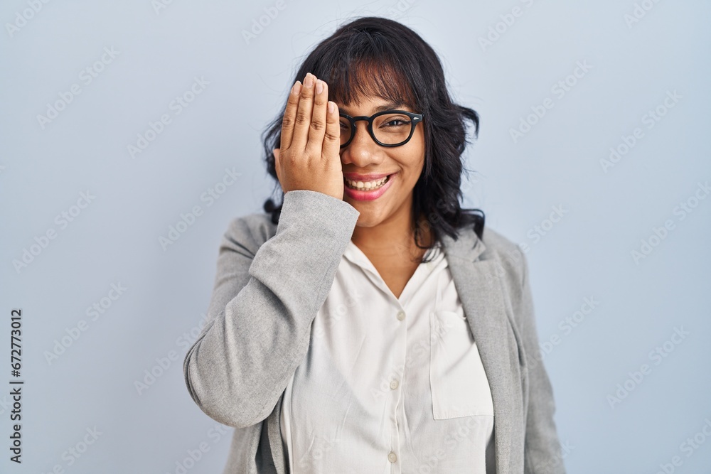 Hispanic woman standing over isolated background covering one eye with hand, confident smile on face and surprise emotion. Hispanic woman standing over isolated background covering one eye with hand, confident smile on face and surprise emotion.