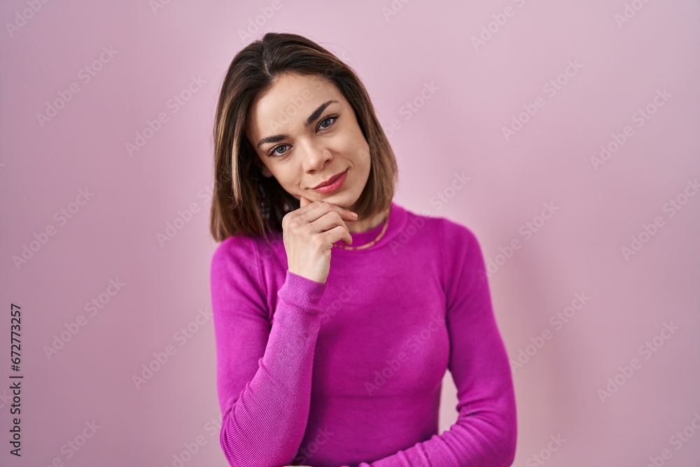 Hispanic woman standing over pink background looking confident at the camera smiling with crossed arms and hand raised on chin. thinking positive. Hispanic woman standing over pink background looking confident at the camera smiling with crossed arms and hand raised on chin. thinking positive.