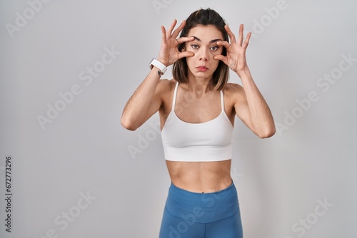 Hispanic woman wearing sportswear over isolated background trying to open eyes with fingers, sleepy and tired for morning fatigue photo