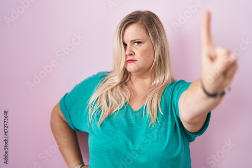 Caucasian plus size woman standing over pink background pointing with finger up and angry expression  showing no gesture