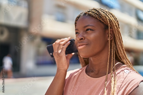 African american woman miling confident listening audio message by the smartphone at street