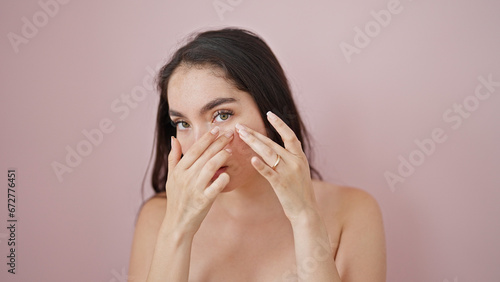 Fotografie Young beautiful hispanic woman popping pimple over isolated pink background