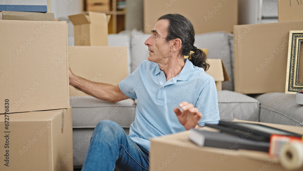 Middle age man sitting on floor looking around at new home Middle age man sitting on floor looking around at new home