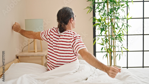 Middle age man waking up stretching arms at bedroom