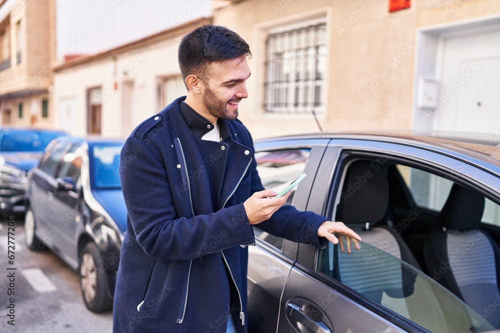 Young hispanic man using smartphone leaning on car at street