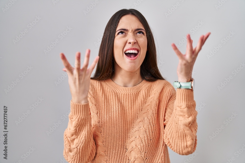 Young brunette woman standing over white background crazy and mad shouting and yelling with aggressive expression and arms raised. frustration concept. Young brunette woman standing over white background crazy and mad shouting and yelling with aggressive expression and arms raised. frustration concept.
