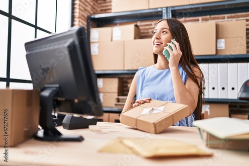Young beautiful hispanic woman ecommerce business worker talking on smartphone holding package at office