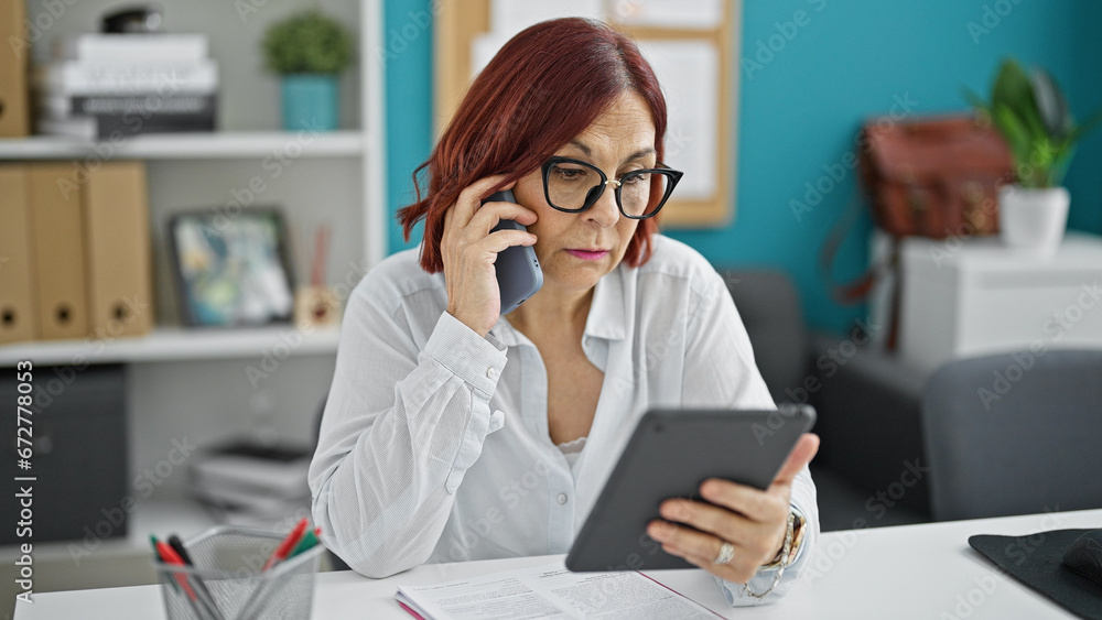 Middle age woman business worker using touchpad talking on smartphone at the office Middle age woman business worker using touchpad talking on smartphone at the office