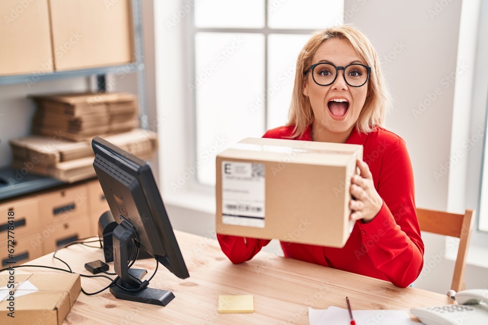 Blonde woman working at small business ecommerce holding box celebrating crazy and amazed for success with open eyes screaming excited. Blonde woman working at small business ecommerce holding box celebrating crazy and amazed for success with open eyes screaming excited.