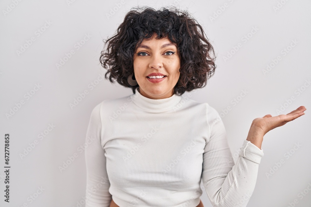 Hispanic woman with curly hair standing over isolated background smiling cheerful presenting and pointing with palm of hand looking at the camera. Hispanic woman with curly hair standing over isolated background smiling cheerful presenting and pointing with palm of hand looking at the camera.