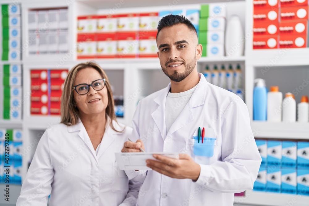 Man and woman pharmacist smiling confident reading prescription at pharmacy