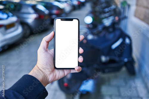 Fototapeta Naklejka Na Ścianę i Meble -  Man holding smartphone showing white blank screen at motorbike parking