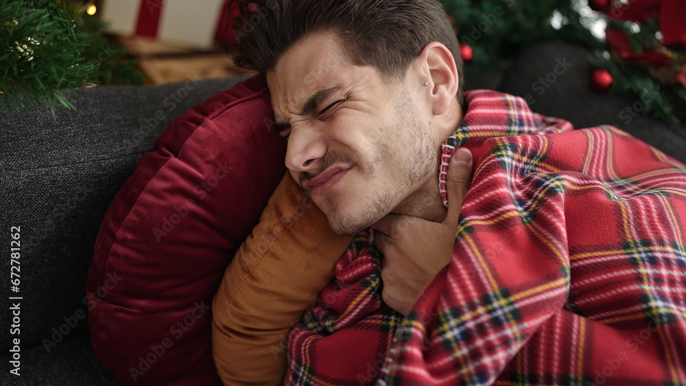 Obraz premium Young hispanic man suffering for throat pain lying on sofa by christmas tree at home