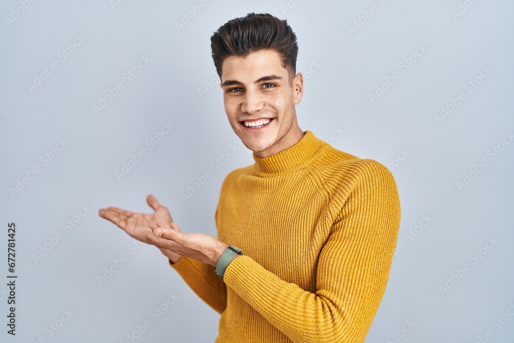 Young hispanic man standing over blue background inviting to enter smiling natural with open hand Young hispanic man standing over blue background inviting to enter smiling natural with open hand