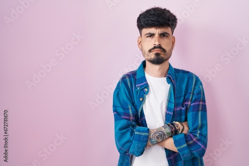 Konstfotografi Young hispanic man with beard standing over pink background skeptic and nervous, disapproving expression on face with crossed arms