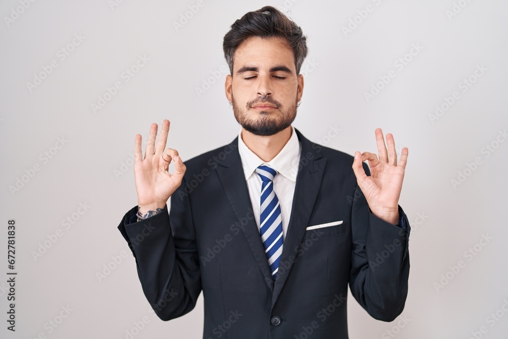 Young hispanic man with tattoos wearing business suit and tie relaxed and smiling with eyes closed doing meditation gesture with fingers. yoga concept. Young hispanic man with tattoos wearing business suit and tie relaxed and smiling with eyes closed doing meditation gesture with fingers. yoga concept.