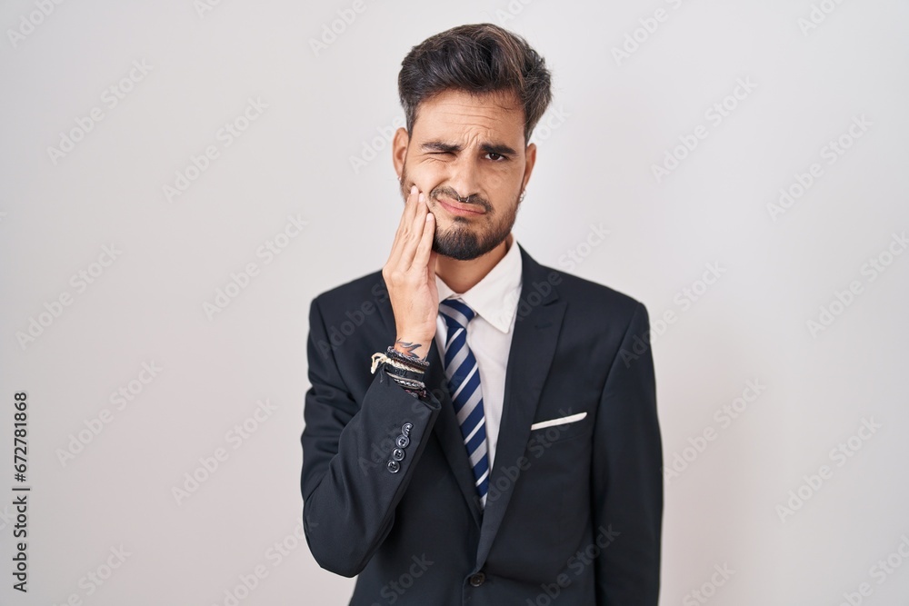 Young hispanic man with tattoos wearing business suit and tie touching mouth with hand with painful expression because of toothache or dental illness on teeth. dentist Young hispanic man with tattoos wearing business suit and tie touching mouth with hand with painful expression because of toothache or dental illness on teeth. dentist