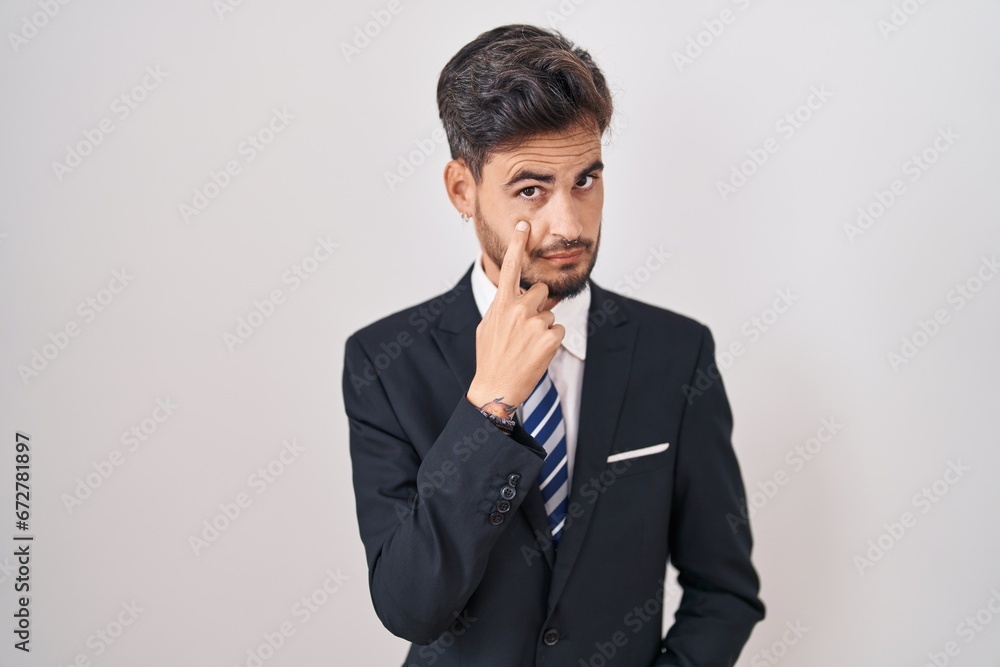 Young hispanic man with tattoos wearing business suit and tie pointing to the eye watching you gesture, suspicious expression Young hispanic man with tattoos wearing business suit and tie pointing to the eye watching you gesture, suspicious expression