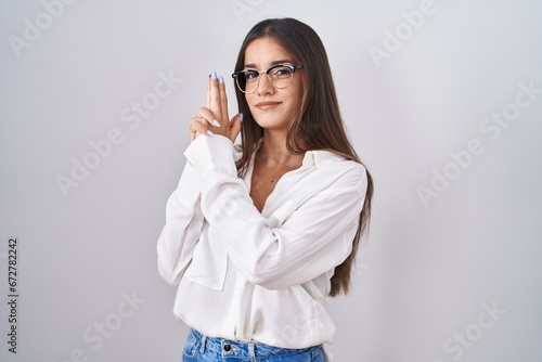 Young brunette woman wearing glasses holding symbolic gun with hand gesture, playing killing shooting weapons, angry face