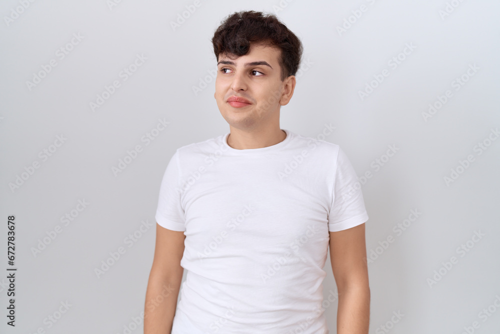 Young non binary man wearing casual white t shirt smiling looking to the side and staring away thinking. Young non binary man wearing casual white t shirt smiling looking to the side and staring away thinking.