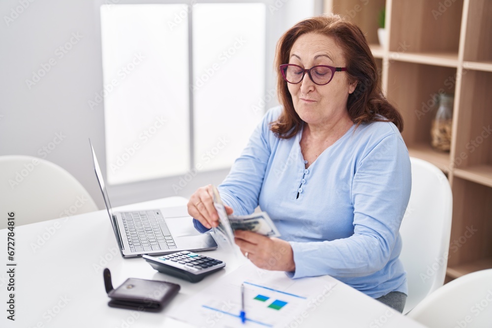 Senior woman using laptop counting dollars at home Senior woman using laptop counting dollars at home