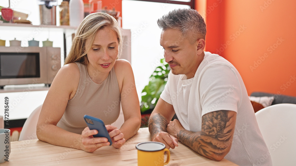 Man and woman couple using smartphone sitting on table at dinning room Man and woman couple using smartphone sitting on table at dinning room