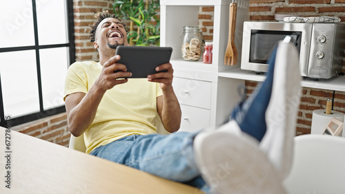 Canvas Print African american man watching video on touchpad laughing a lot at dinning room