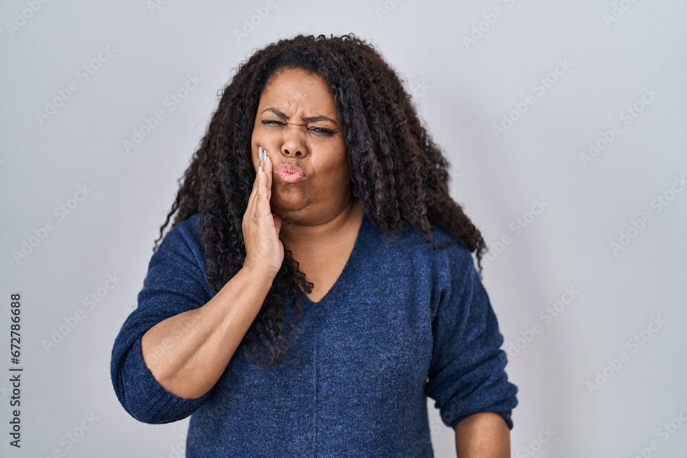 Plus size hispanic woman standing over white background touching mouth with hand with painful expression because of toothache or dental illness on teeth. dentist Plus size hispanic woman standing over white background touching mouth with hand with painful expression because of toothache or dental illness on teeth. dentist
