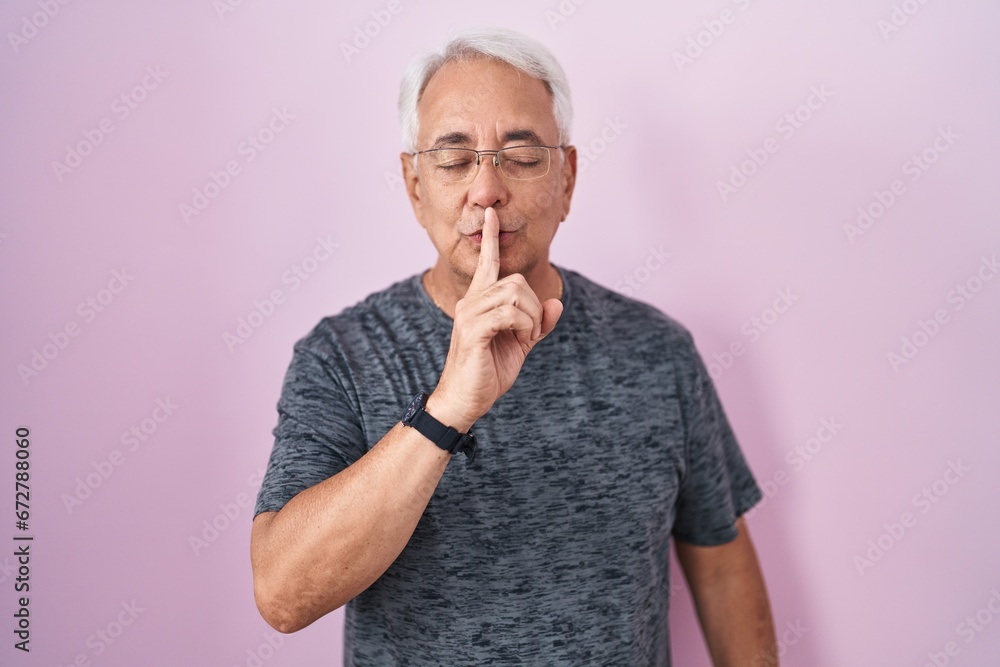 Middle age man with grey hair standing over pink background asking to be quiet with finger on lips. silence and secret concept. Middle age man with grey hair standing over pink background asking to be quiet with finger on lips. silence and secret concept.