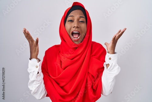 Young arab woman wearing traditional islamic hijab scarf celebrating mad and crazy for success with arms raised and closed eyes screaming excited. winner concept