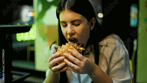 Young beautiful hispanic woman eating delicious hamburger at the restaurant