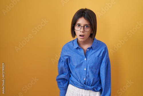 Young girl standing over yellow background in shock face, looking skeptical and sarcastic, surprised with open mouth © Krakenimages.com