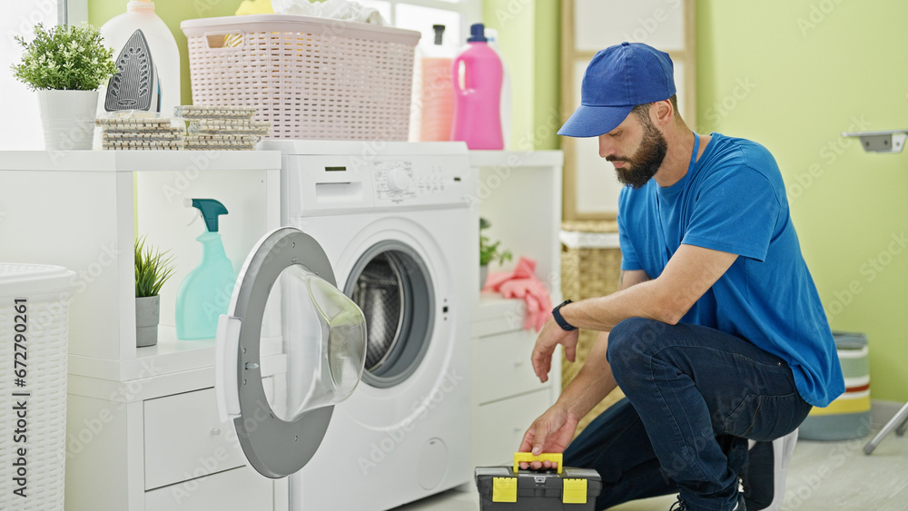 Young hispanic man technician repairing washing machine at laundry room - obrazy, fototapety, plakaty 