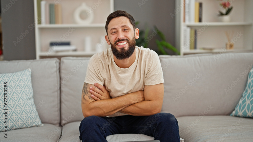 Young hispanic man smiling confident sitting on sofa with arms crossed gesture at home