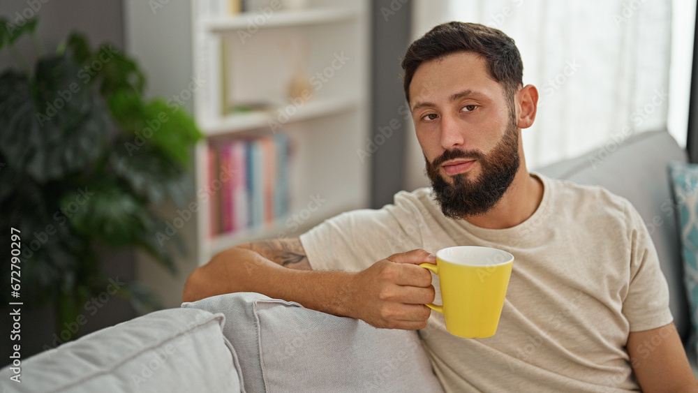 Young hispanic man drinking coffee sitting on sofa at home Young hispanic man drinking coffee sitting on sofa at home