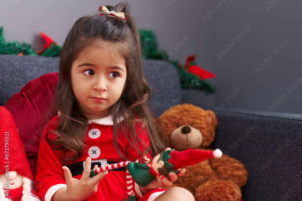 Adorable hispanic girl playing with elf toy sitting on sofa by christmas decoration at home Adorable hispanic girl playing with elf toy sitting on sofa by christmas decoration at home