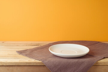Empty white plate with tablecloth on wooden table over orange wall background. Thanksgiving  mock up for design and product display