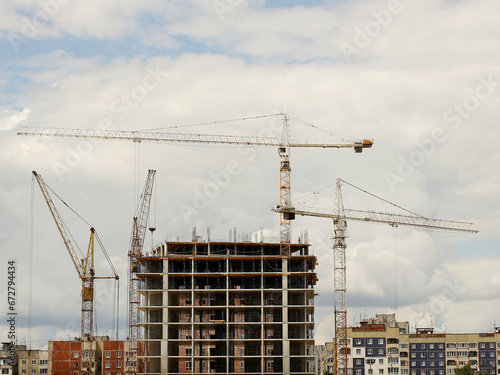 Tower cranes work during the construction of a multi-story building. New apartments for residents and premises for offices. Risky work at height. Lifting heavy building materials. City development