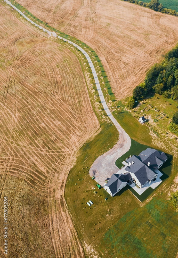 Aerial shot of a large two-story house stands in a vast grassy field in a rural area