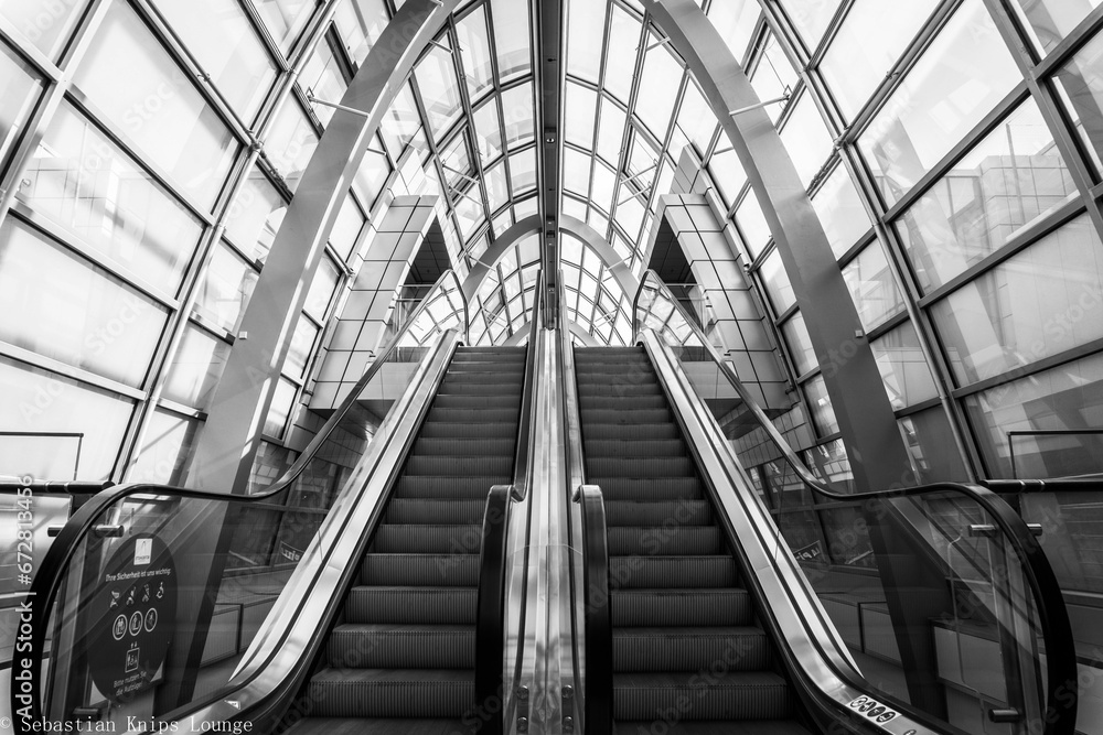 Black and white shot of escalators traveling in a downward direction in a commercial building Black and white shot of escalators traveling in a downward direction in a commercial building