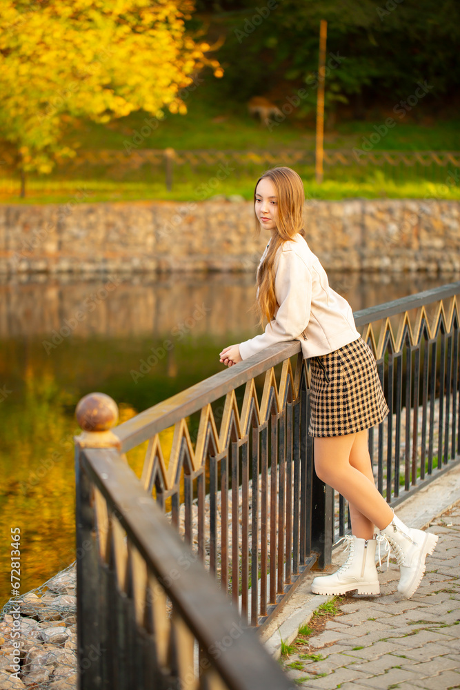 A young smiling girl walking in an autumn park in a good mood. Teenage girl, portrait against a background of nature. Fashion style trend.