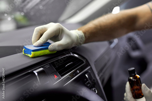 cropped male auto service worker in protective gloves, applying special polish cream on rag and polish interior of car, in renew service station shop