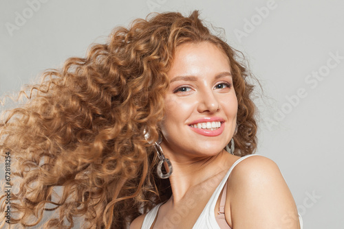 Attractive woman redhead fashion model with long natural healthy brown curly hair and cute smile laughing on white background. Hair care, hair treatment, wellness, joy and cosmetology concept