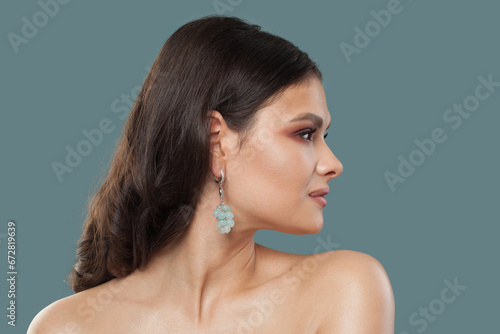 Pretty stylish lady portrait. Brunette woman in gold jewelry earring posing on blue background