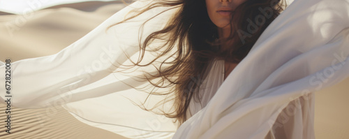 Woman in a long white dress walking in the desert with flowing fabric in the wind