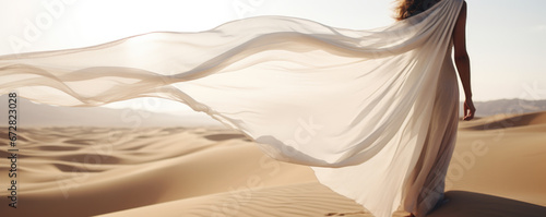 Woman in a long white dress walking in the desert with flowing fabric in the wind