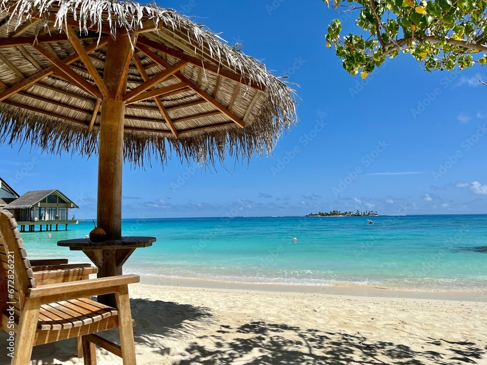 Fototapeta premium a wooden chair sits under an umbrella on a sandy beach
