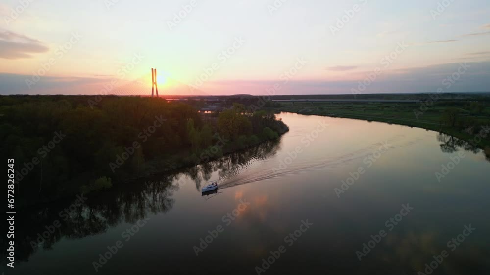 Aerial of a boat sailing in the waters of the lake with a bridge and the sunset in the background Aerial of a boat sailing in the waters of the lake with a bridge and the sunset in the background