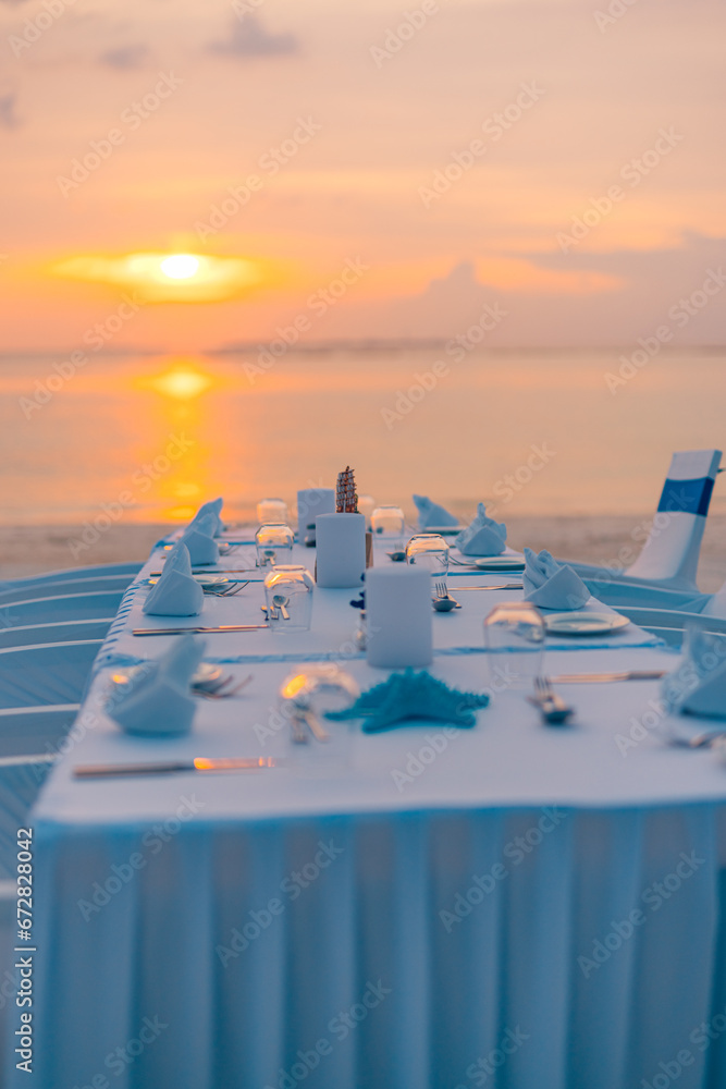 Obraz premium Concept of a tropical destination wedding in front of the ocean. Beautiful wedding arch on the beach. Table setting at a luxury wedding and Beautiful flowers on the table. Dream sunset decoration